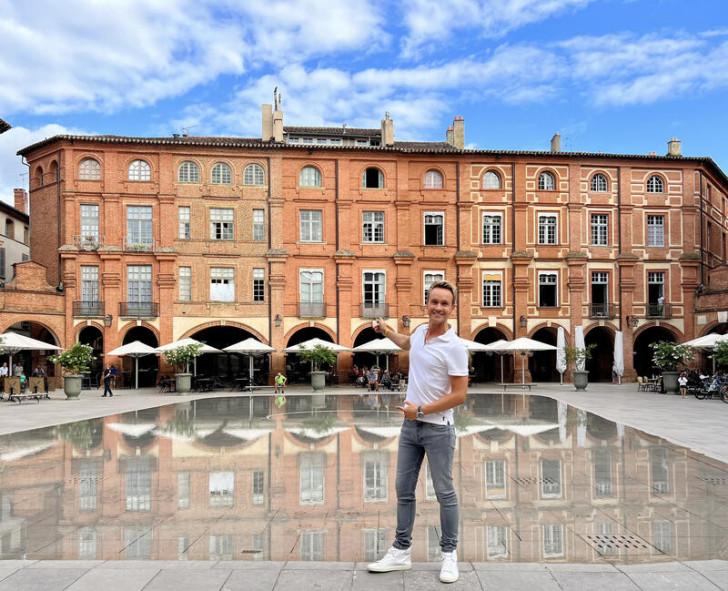 Cyril Féraud désignant de la main droite les façades rouges d'une place de Montauban 